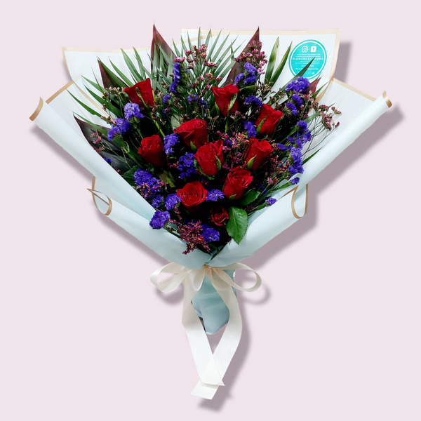 A big bouquet, featuring a mix of purple and red roses and green foliage, wrapped in paper with a ribbon.