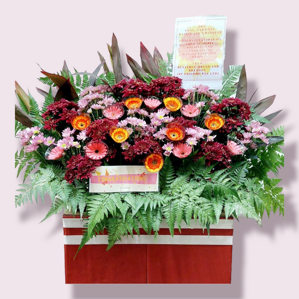 A 110cm tall box stand with an assortment of brightly colored flowers, ferns, leaves & ribbons, including a laminated A4 sized card with a message.