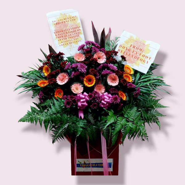 A 110cm tall box stand with an assortment of brightly colored flowers, ferns, leaves & ribbons, including a laminated A4 sized card with a message.